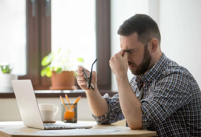 Tired stressed male worker taking off glasses, person massaging nose bridge suffering from headache and trying to relieve pain. Despaired man frustrated after reading company collapse or failure news