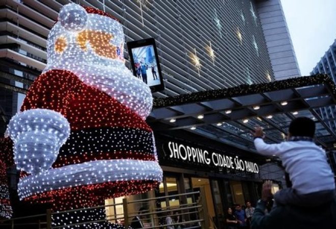 Pai e criança tiram foto com Papai Noel gigante em frente a shopping em São Paulo