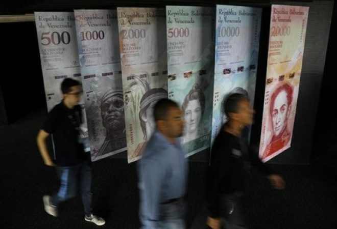 Pessoas  passam por cartazes do bolívar venezuelano no prédio do Banco Central em Caracas, Venezuela