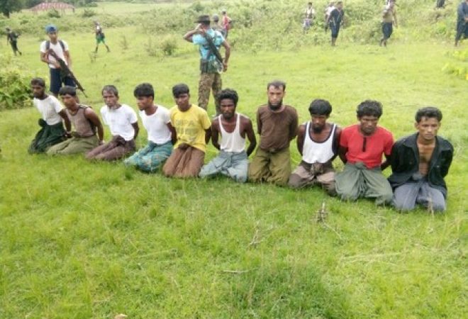 Dez muçulmanos rohingya são vistos ajoelhados e com mãos amarradas ao lado de membros das Forças de Segurança de Mianmar em  Inn Din