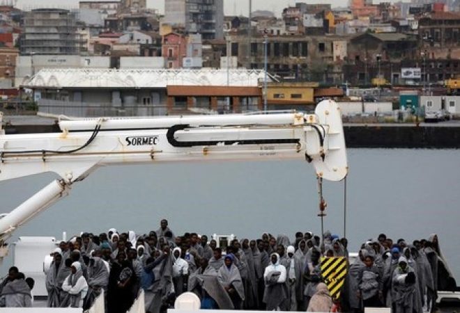 Imigrantes aguardam para desembarcar de embarcação da Guarda Costeira italiana em porto da Sicília