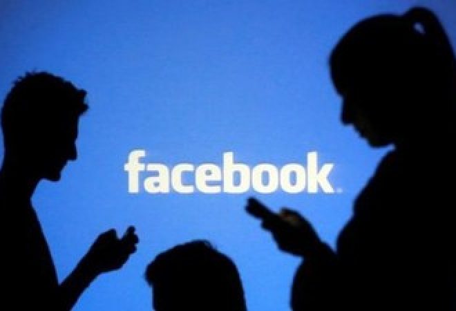 Pessoas utilizam celulares diante de projeção do logo do Facebook em foto ilustrativa