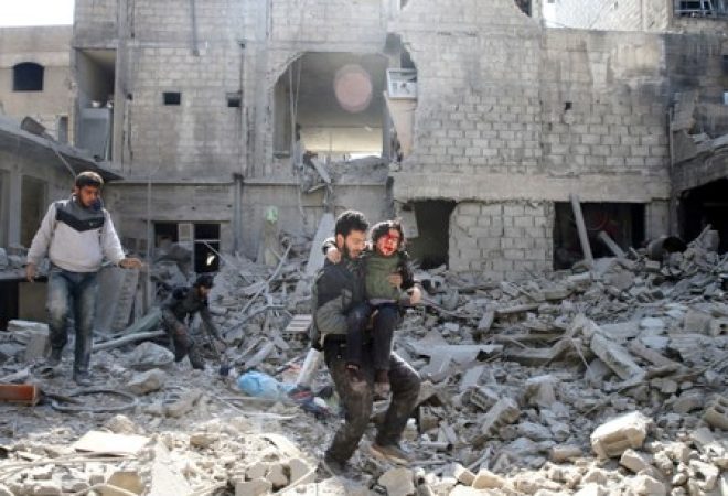 Homem carrega menino ferido em meio a destroços na cidade de Hamouriyeh, em Ghouta Oriental, na Síria