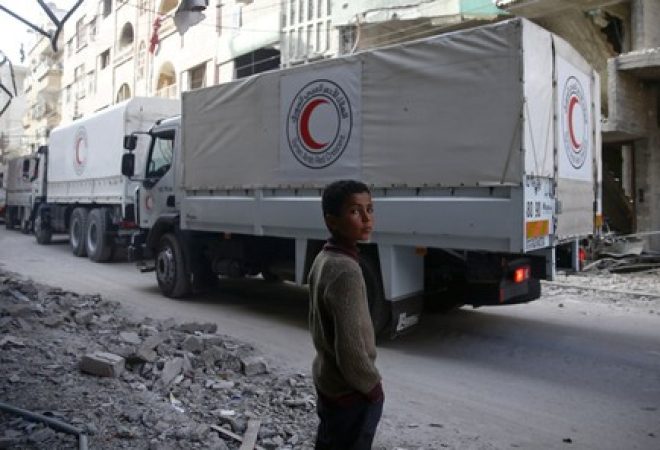Menino é visto ao lado de comboio de ajuda humanitária do Crescente Vermelho na cidade de Douma, em Ghouta Oriental, na Síria