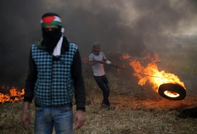 Manifestante palestino move pneu em chamas durante confronto com soldados israelenses na fronteira entre Israel e Gaza