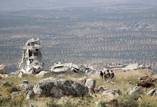 Combatentes rebeldes caminham por montanha com vista para a cidade de Ariha, na província de Idlib, na Síria