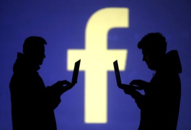 Pessoas usam computadores diante de projeção do logo do Facebook em foto ilustativa