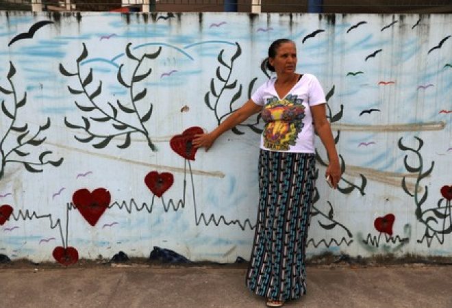 Rosilene Alves aponta para buracos de bala em muro da escola onde sua filha foi baleada em 2017, no Rio de Janeiro