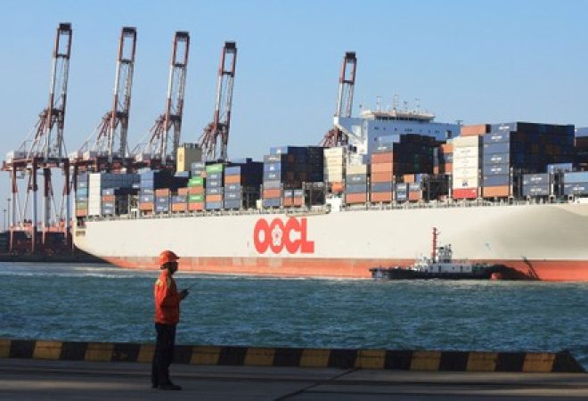 Trabalhador em frente a um navio de contêineres Orient Overseas Container Line (OOCL) em um porto em Qingdao