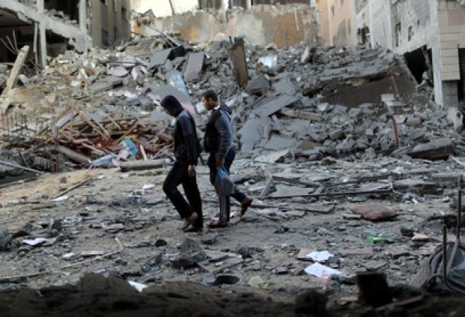 Palestinos passam por destroços de prédio destruído por ataque aéreo israelense em Gaza