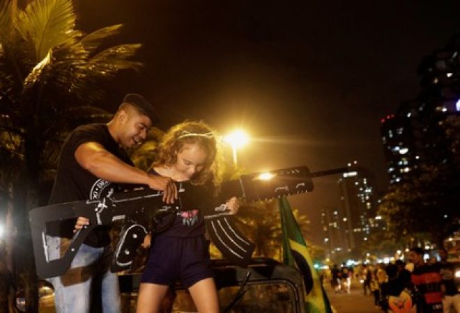 Apoiador de Bolsonaro ajuda menina a segurar arma de papelão, no Rio de Janeiro