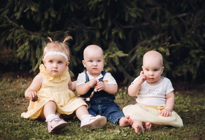 Three adorable nice babies wearing in spring clothes while looking at camera in the garden. Happy childhood concept