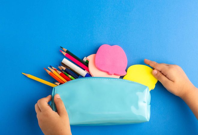 top-view-little-kid-holding-blue-pen-box-full-colorful-pencils-blue-surface