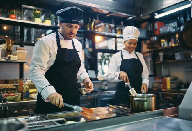 Male chef and his African American female coworker preparing food in a restaurant.