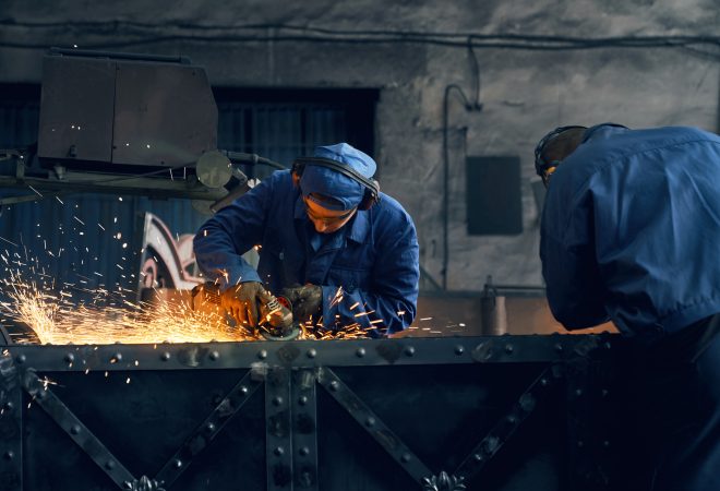 Front view of two men working with special electric steel cutter machine for welding or making gates in smithy. Concept of process produce modern fence in garage.