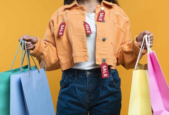 vista-frontal-de-uma-mulher-vestindo-uma-jaqueta-com-etiquetas-e-segurando-sacolas-de-compras
