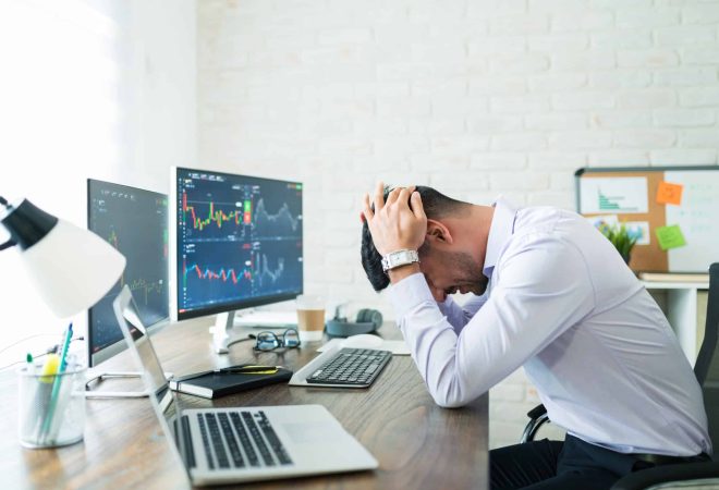 Side view of stressed young broker sitting with head in hands at desk while working from home