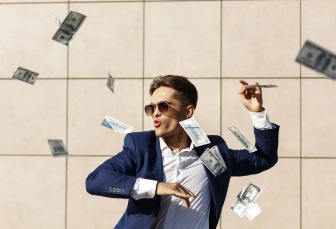 Young businessman throughs around dollars and dances on the street