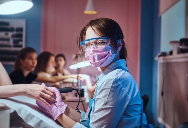 Young cheerful manicure master at her own workplace with client is working on woman's nails.