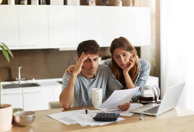 Unhappy American couple managing home accounts in kitchen, trying to save some money by cutting family expenses. Finances, bankruptcy, taxes, money, accounting and financial problems concept