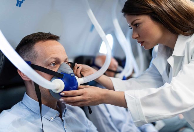 Young doctor assisting patient with a mask during hyperbaric oxygen therapy at clinic.