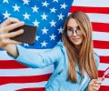 Tsu is the US Independence Day! Young pretty American girl doing selfie against the background of the flag.