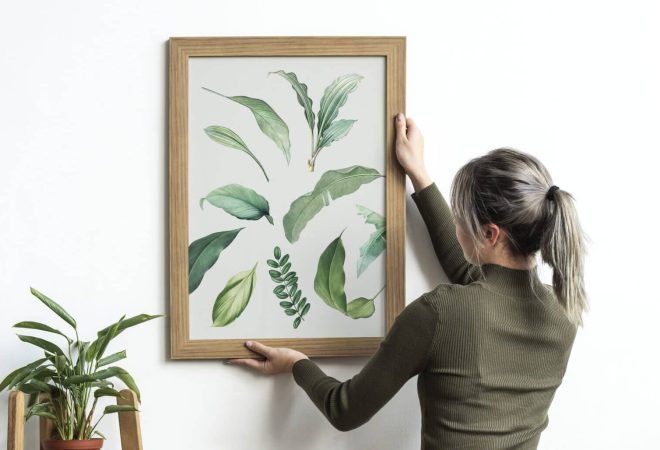 Young woman hanging a frame of leaf print painting on the wall